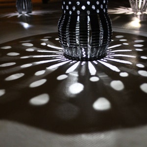 May include: A close-up of a patterned metal lampshade casting a shadow of light and dark circles on a surface.