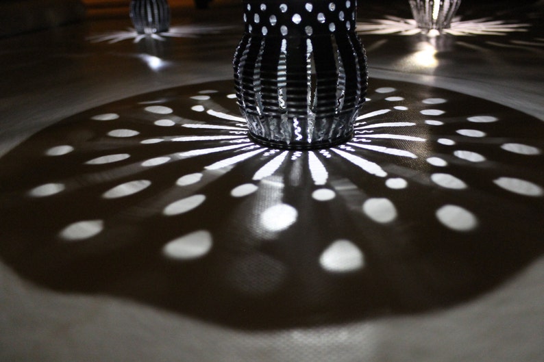 May include: A close-up of a patterned metal lampshade casting a shadow of light and dark circles on a surface.