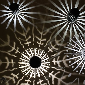May include: Four black metal ceiling lights with white geometric designs cast on the ceiling. The lights are round and have a starburst pattern.