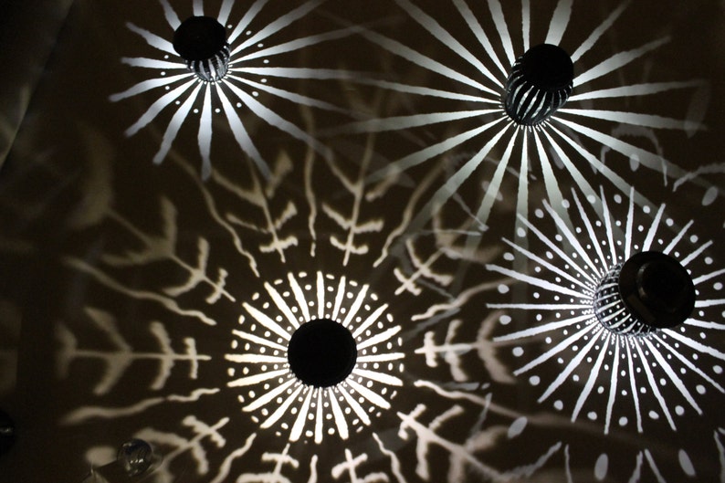 May include: Four black metal ceiling lights with white geometric designs cast on the ceiling. The lights are round and have a starburst pattern.