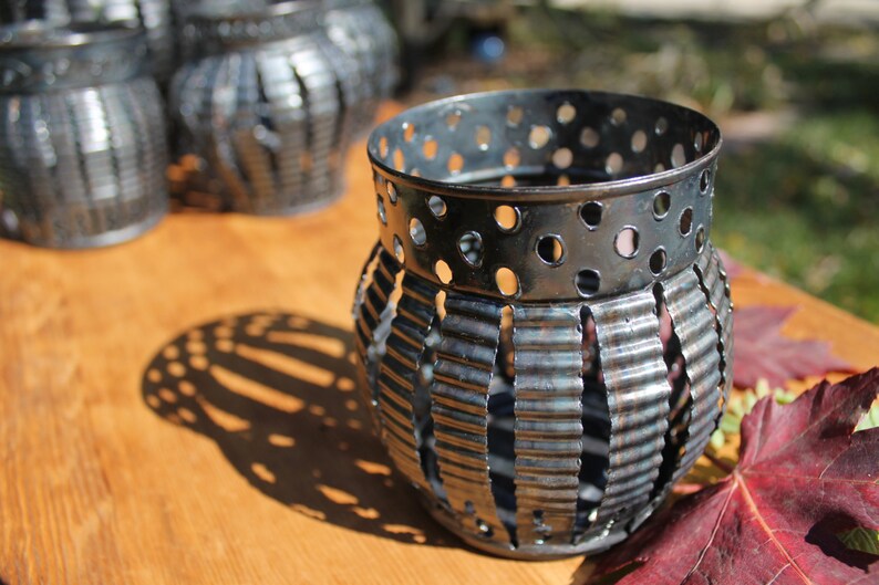 May include: A set of four black metal candle holders with a decorative, textured design. The candle holders are made of recycled materials and have a rustic, vintage look.