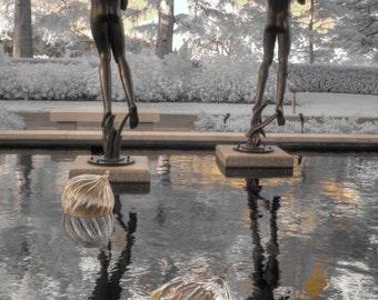 May include: Two bronze sculptures of people standing in a reflecting pool with two round, metallic objects in the water.