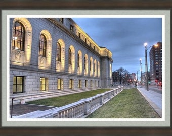 May include: A large, stone building with many windows and a long, low facade. The building is lit up at night, and there is a grassy area in front of it. The building is located on a street with other buildings in the background.