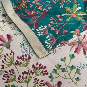 May include: Close-up of a teal fabric with a floral pattern. The fabric has a white border and is folded over a pink fabric with a similar floral pattern.