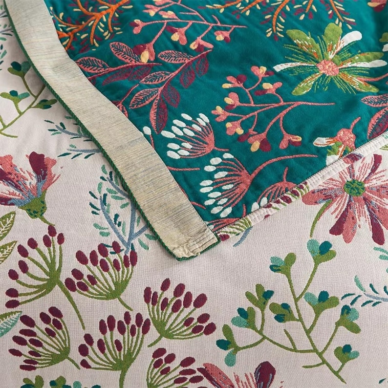 May include: Close-up of a teal fabric with a floral pattern. The fabric has a white border and is folded over a pink fabric with a similar floral pattern.