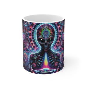 May include: A white ceramic mug with a colorful psychedelic design featuring an alien with glowing eyes and a third eye. The alien is surrounded by a swirling pattern of colors and shapes.