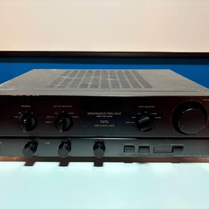 May include: Black Sony F270 stereo amplifier with multiple knobs and buttons. The amplifier has the words "SPONTANEOUS TWIN DRIVE" and "SUPER LEGATO CIRCUIT" printed on the front. The amplifier is sitting on a white surface.