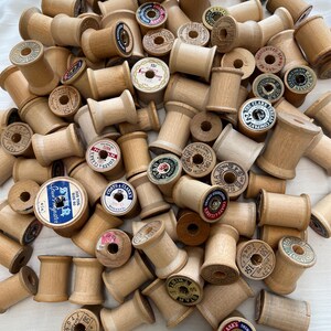 May include: A collection of vintage wooden spools, some with printed labels in various colors. The spools are in various sizes and are made of light-colored wood. Some labels include text like "STAR" and "COATS & CLARK'S".