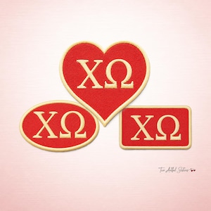 May include: Three embroidered patches in red with the Greek letters ΧΩ in a cream color. The patches are in the shapes of a heart, an oval, and a rectangle. The patches have a cream-colored border. The background is a light pink.
