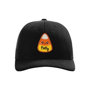 Peut inclure: Casquette de baseball noire avec un dos en filet et un &eacute;cusson en forme de bonbon de ma&iuml;s. L'&eacute;cusson repr&eacute;sente un bonbon de ma&iuml;s souriant avec le nom "Billy" en &eacute;criture cursive. La casquette a une visi&egrave;re incurv&eacute;e et un bouton sur le dessus.