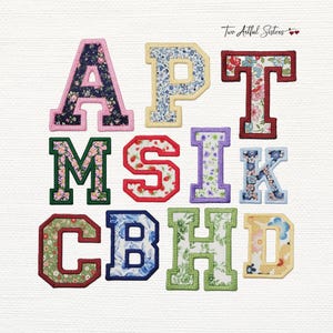 May include: A collection of eleven fabric letter patches featuring various floral patterns and solid-colored stitched borders. The letters include A, P, T, M, S, I, K, C, B, H, and D, each with a distinct textile design and embroidered edge.