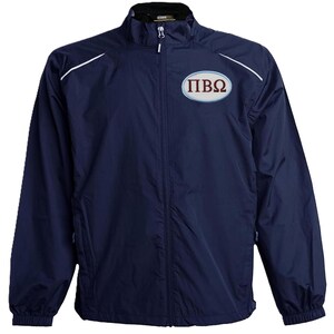 May include: A navy blue zip-up jacket with white shoulder trim and a small chest logo. The logo features the Greek letters &Pi;, I, and &Omega; in maroon. The jacket has a stand-up collar.