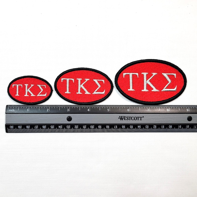 May include: Three red oval patches with the Greek letters TKS in white, each with a black border. A ruler with inch measurements is below the patches, showing their varying sizes.