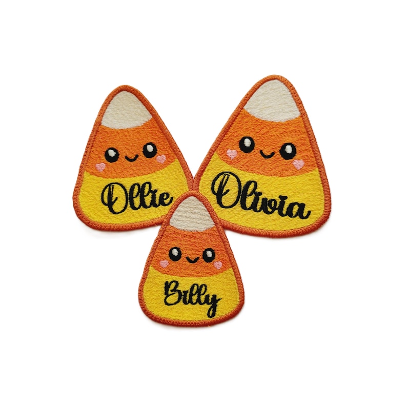 Peut inclure: Trois &eacute;cussons brod&eacute;s en forme de bonbons de ma&iuml;s avec des visages souriants et les noms : Ollie, Olivia et Billy. Les &eacute;cussons pr&eacute;sentent un dessus blanc, un milieu orange et un bas jaune, avec une bordure rouge.