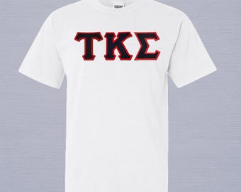 Könnte beinhalten: Ein weißes kurzärmeliges T-Shirt mit Rundhalsausschnitt und den griechischen Buchstaben TKE in Schwarz mit roter Umrandung mittig auf der Brust. Das Shirt hat eine Standardpassform mit geripptem Kragen und einem kleinen Markenetikett am Innenhals.