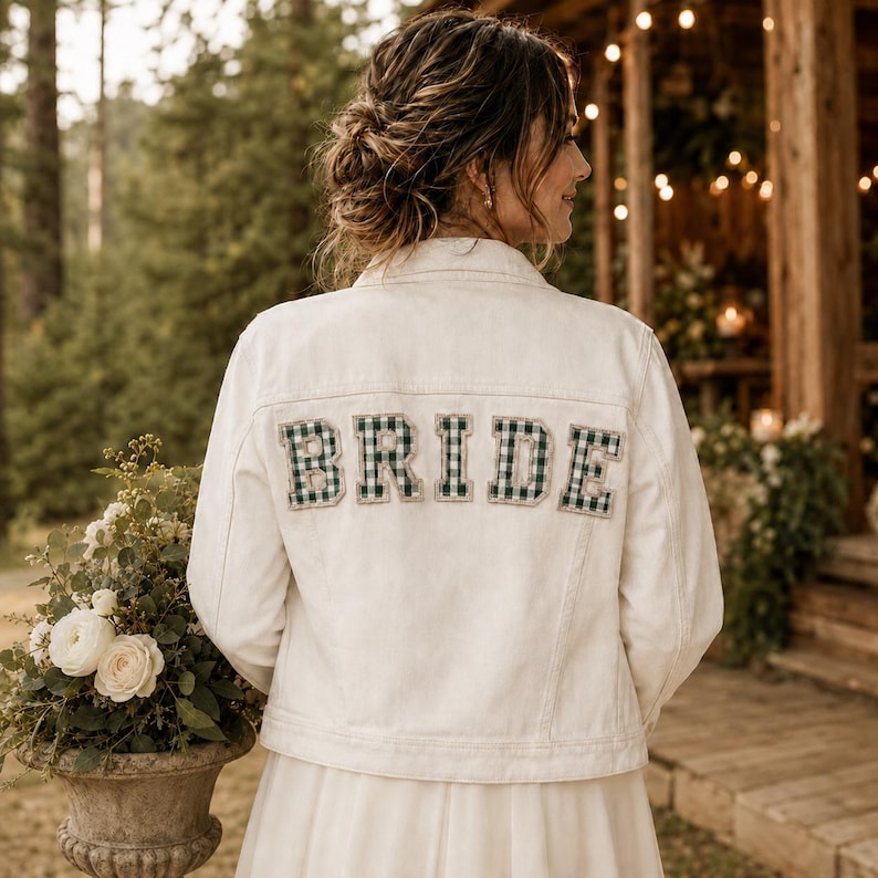 K&ouml;nnte beinhalten: Eine wei&szlig;e Jeansjacke mit dem Wort BRIDE in gro&szlig;en Blockbuchstaben auf dem R&uuml;cken. Die Buchstaben sind mit einem dunkelgr&uuml;n-wei&szlig;en Vichy-Karomuster gef&uuml;llt und mit einem hellen Stoffrand eingefasst.