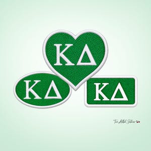 May include: Three embroidered patches in green with white borders and white Greek letters Kappa Delta. The set includes one heart-shaped patch, one oval-shaped patch, and one rectangular-shaped patch, all featuring the same Greek letter design.