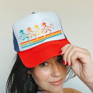 Peut inclure: Casquette de camionneur rouge, blanche et bleue marine avec un motif coloré de personnages dansants et le texte "WSMFP". Le chapeau a un dos en filet et une visière incurvée. Le design comprend une bande arc-en-ciel.
