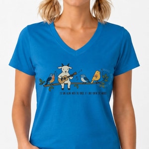Op de afbeelding: Een felblauw T-shirt met V-hals voorzien van een afbeelding van een witte geit die gitaar speelt op een tak met drie kleurrijke vogels. De tekst onder de illustratie luidt: I'D SING ALONG WITH THE BIRDS, IF I ONLY KNEW THE WORDS.