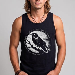May include: A black tank top featuring a circular graphic of a crow perched on a branch. The text surrounding the crow reads, "IT'S THE SAME STORY THE CROW TOLD ME IT'S THE ONLY ONE HE KNOWS." The design is rendered in white ink on the dark fabric.