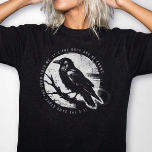 May include: A black short-sleeved t-shirt featuring a white circular graphic of a crow perched on a branch. The text surrounding the crow reads, "IT'S THE SAME STORY THE CROW TOLD ME IT'S THE ONLY ONE HE KNOWS" in a circular sans-serif font.