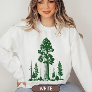 Può includere: Felpa bianca con una grafica verde di un albero alto e alberi più piccoli. Il testo "WHITE" è in basso. Il design è un'illustrazione a tema natura.