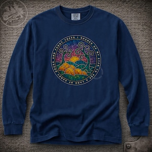May include: A navy blue long-sleeve shirt featuring a circular graphic with a stained-glass style landscape of trees, hills, and a sun. The text surrounding the design reads, "AND FUNNY TREES I OPENED UP MY EYES TO SEE A LAND OF SUNNY ROCKS."