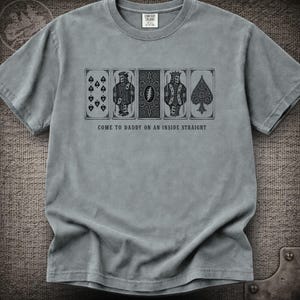 May include: A grey short-sleeve t-shirt featuring a graphic print of five playing cards in a row. The design includes skeletons and the text "COME TO DADDY ON AN INSIDE STRAIGHT" printed in black ink. The shirt has a crew neckline and a tag at the collar.