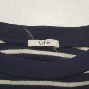 May include: Close-up of a navy blue and white striped top. The top has a ribbed texture and a rounded neckline. A small tag with the text "Y's bis" is sewn into the neckline. The fabric appears to be a soft knit.