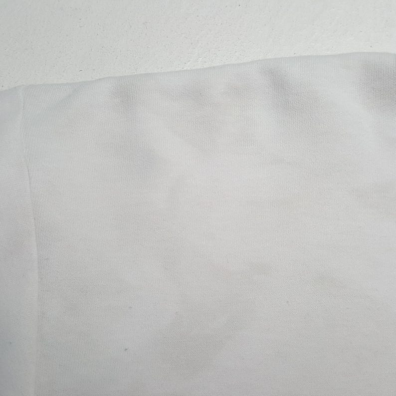 May include: Close-up of a white fabric, possibly a section of a garment. The fabric appears to be a soft, textured material, with subtle variations in tone and slight imperfections.