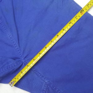 May include: Close-up of blue fabric with a yellow measuring tape. The tape shows measurements in inches, highlighting the texture and color of the material. The fabric appears to be part of a garment.