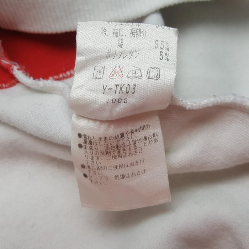 May include: Close-up of a white fabric tag with Japanese text and care symbols. The tag indicates the fabric composition is 95% cotton and 5% polyurethane. The tag also has the text "Y-TK03" and "1002".