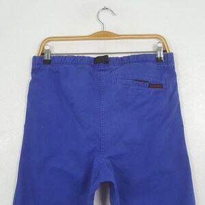 May include: Bright blue shorts with an elastic waistband and a small back pocket. The shorts are hanging on a wooden hanger against a white background. The back pocket has a small red and white logo.