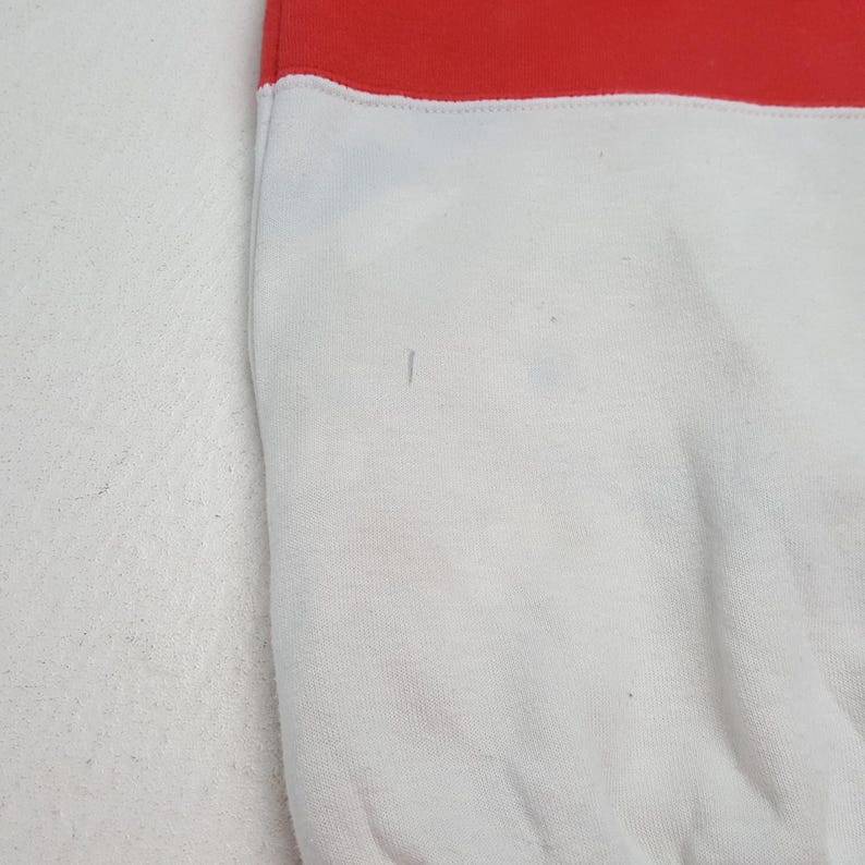 May include: A close-up of a white and red sweatshirt. The top portion is red, and the bottom is white. The fabric appears to be a soft material. There are a few small marks on the white portion of the sweatshirt.