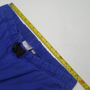 May include: Close-up of blue pants with an elastic waistband. A black buckle and a tag with the text "ORIGINAL FREEDOM USA" are visible. A yellow measuring tape is placed across the pants, showing measurements in inches.