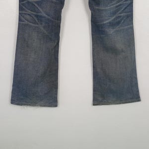 May include: Faded blue denim jeans with a straight leg cut. The jeans show wear and tear with visible fading and distressed areas. The denim has a classic five-pocket design.