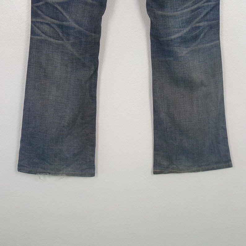 May include: Faded blue denim jeans with a straight leg cut. The jeans show wear and tear with visible fading and distressed areas. The denim has a classic five-pocket design.