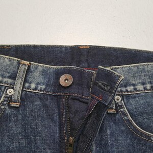 May include: Close-up of a pair of blue denim jeans. The image shows the button, zipper, and stitching details. The jeans have a classic five-pocket design with a metal button closure and a zipper fly.