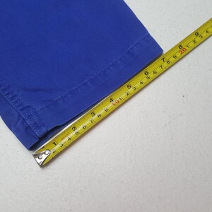 May include: Close-up of a section of bright blue fabric with a yellow measuring tape. The tape shows measurements in inches, with the fabric's edge visible. The fabric is a solid, vibrant blue.