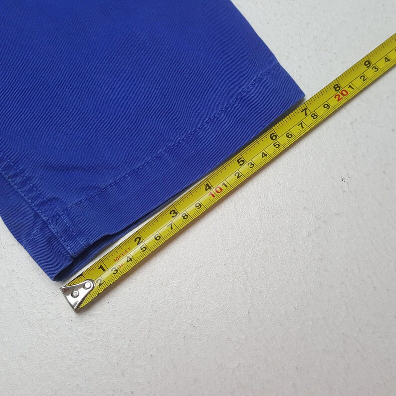 May include: Close-up of a section of bright blue fabric with a yellow measuring tape. The tape shows measurements in inches, with the fabric's edge visible. The fabric is a solid, vibrant blue.