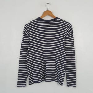 May include: A long-sleeved shirt with horizontal navy blue and white stripes. The shirt is hanging on a wooden hanger against a white background. The shirt has a crew neck and a relaxed fit.