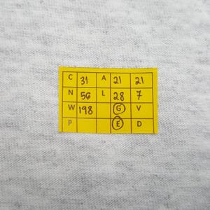 May include: A close-up of a yellow sticky note with black text and numbers. The note is divided into boxes with the letters C, N, W, P, A, L, G, E, V, and D. The numbers 31, 56, and 198 are visible.