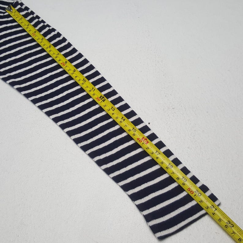 May include: A navy blue and white striped sleeve is measured with a yellow tape measure. The sleeve is made of a knit fabric. The tape measure shows a length of approximately 21 inches.
