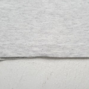 May include: Close-up of a light gray fabric with a subtle speckled pattern. The fabric is folded at the bottom, revealing a seam with visible stitching. The texture appears soft and slightly textured, suggesting a comfortable material.