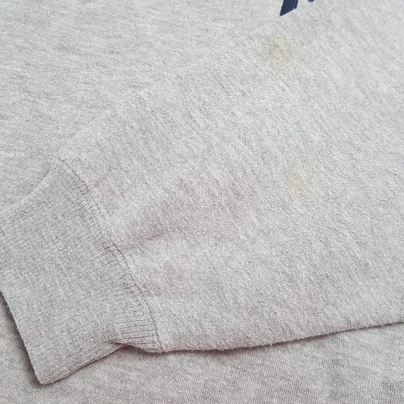 May include: Close-up of a gray sweatshirt sleeve. The cuff is ribbed and the fabric has a slightly worn appearance. There are some light stains on the fabric. The overall look is casual and comfortable.