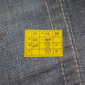 May include: Close-up of blue denim fabric with a yellow tag. The tag has several rows of numbers and letters, including "C 30", "A 16", and "W G10". The denim has visible stitching and a textured surface.