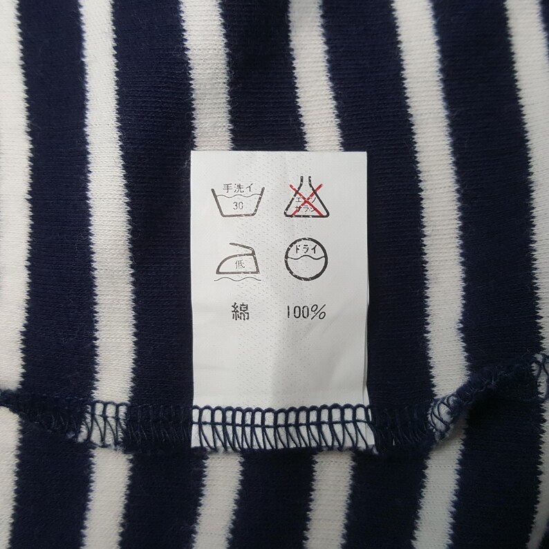 May include: Close-up of a navy blue and white striped fabric. A white tag with Japanese characters and symbols is attached to the fabric. The tag includes washing instructions, such as hand wash at 30 degrees.