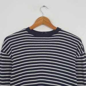 May include: A navy blue and white striped long-sleeve shirt hanging on a wooden hanger. The shirt features horizontal stripes and a crew neck. The garment is made of a soft material and is suitable for casual wear.