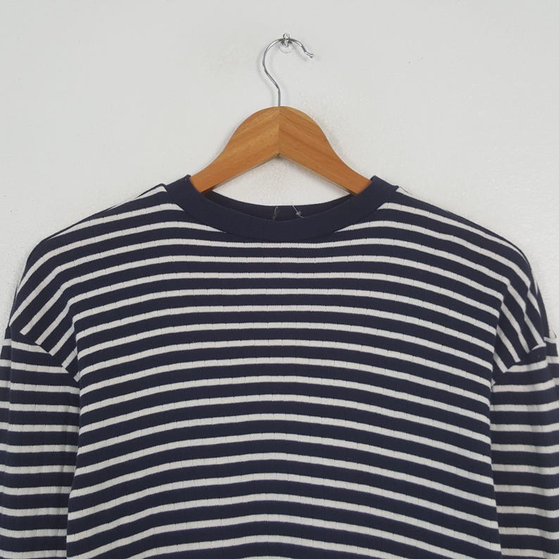 May include: A navy blue and white striped long-sleeve shirt hanging on a wooden hanger. The shirt features horizontal stripes and a crew neck. The garment is made of a soft material and is suitable for casual wear.