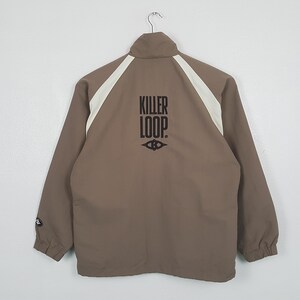 May include: A brown jacket with white shoulder and back panel detailing. The jacket features the black text "KILLER LOOP" on the back. It has a zip closure and long sleeves. The jacket is hanging on a hanger.